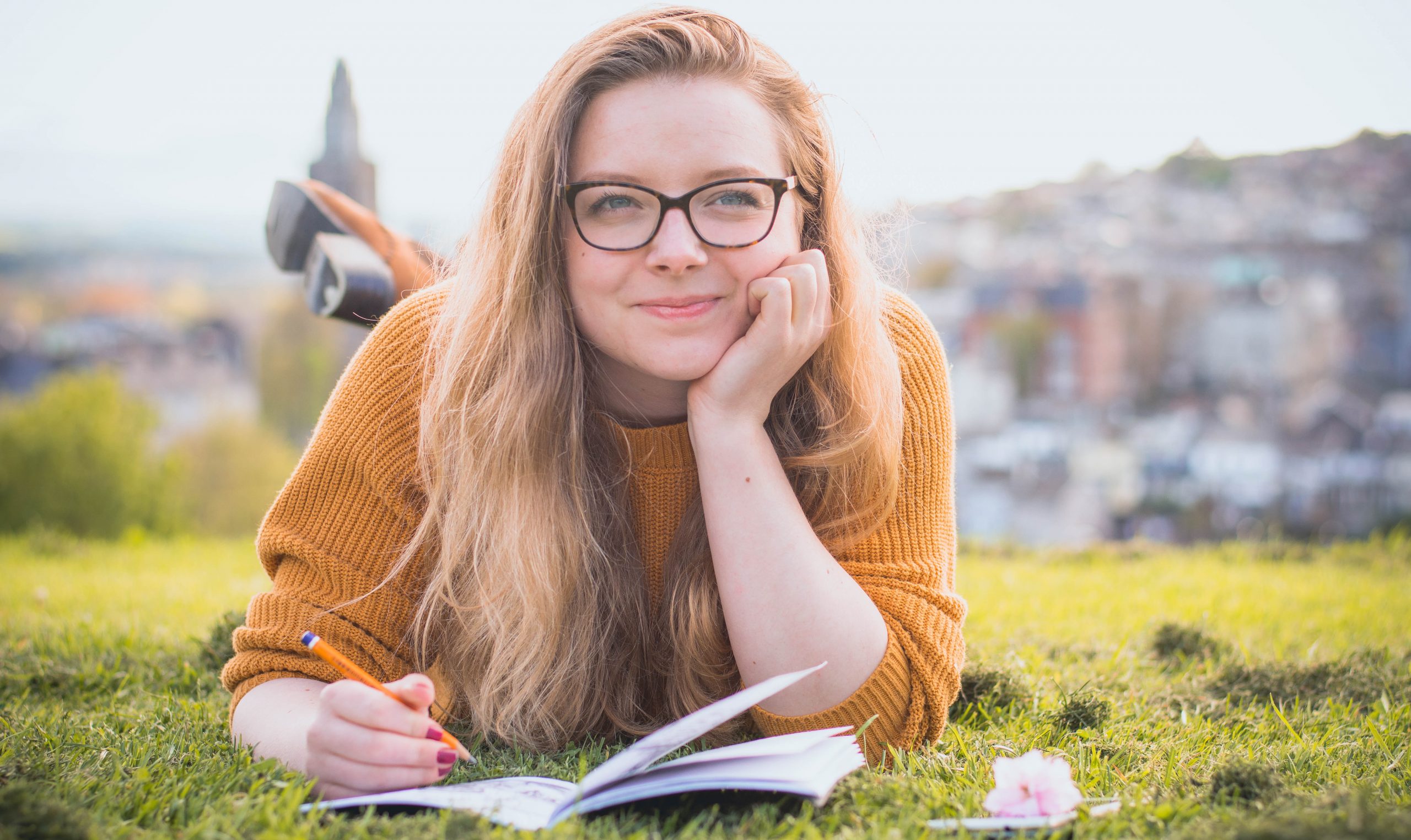 college-woman-lying-on-green-grass-while-holding-pencil-